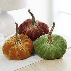 three velvet pumpkins sitting on top of a wooden table next to a white lamp