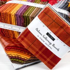 several different colors of fabric are stacked on top of each other with a measuring tape