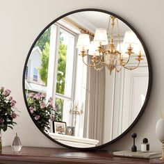 a large round mirror sitting on top of a wooden table next to a vase with flowers