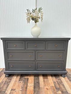 a vase with flowers sitting on top of a gray dresser next to a white wall