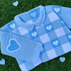 a blue knitted sweater with hearts on it sitting in the grass next to some white hearts