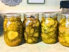 four jars filled with pickles sitting on top of a counter