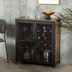 a cabinet with wine bottles and glasses on it next to a chair in front of a potted plant