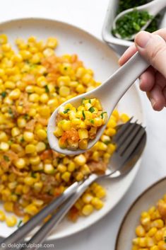 a spoon filled with corn on top of a white plate