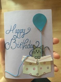 a person holding up a birthday card with a cat in an envelope and a balloon attached to it