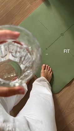 a person is holding a glass with their feet on the floor next to a mat