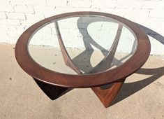 a glass and wood table sitting on top of a cement ground next to a white brick wall