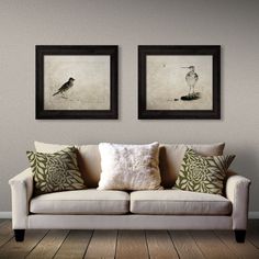 two framed pictures hang on the wall above a couch in a room with wood floors