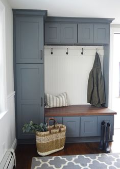 a bench and coat rack in a room with wooden floors, white walls and gray cabinets