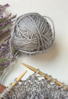 two skeins of yarn are next to some knitting needles and lavender sprigs