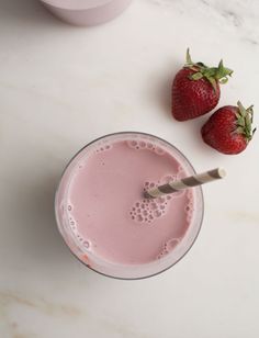 two strawberries sit next to a smoothie in a glass on a marble table