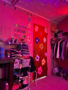 a room filled with lots of clothes and pink lighting on the ceiling above it is a red door that has flowers painted on it