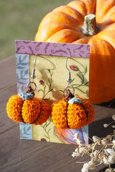 two orange pom - poms hanging from earrings on a table next to pumpkins