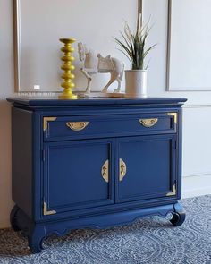 a blue sideboard with gold handles and knobs on it, next to a potted plant