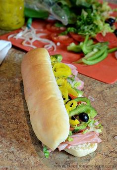 a long sub sandwich sitting on top of a counter next to vegetables and condiments