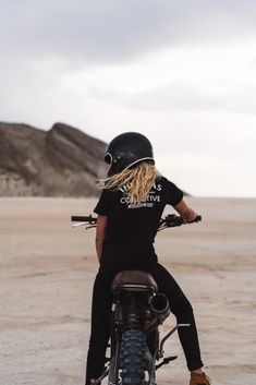 a woman riding on the back of a motorcycle down a sandy beach covered in sand