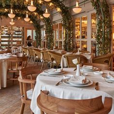 a dining room with tables and chairs covered in white tablecloths, surrounded by greenery