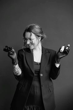 a woman in a black suit holding a camera and wearing gloves with tattoos on her arms