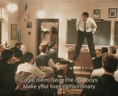 a man standing on top of a desk in front of a classroom full of people