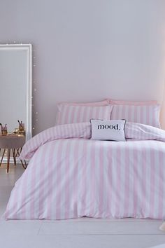 a bed with pink and white striped comforter next to a mirror in a room