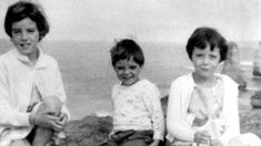 three children are sitting on the rocks by the water and posing for a photo in black and white