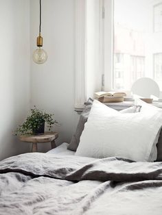 a bed with white sheets and pillows next to a small table with a potted plant on it