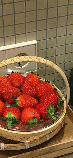 a basket filled with lots of strawberries on top of a wooden table next to a microwave