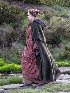 a woman dressed in medieval clothing walking across a field