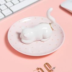 a white cat figurine sitting on top of a plate next to a keyboard