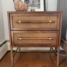 a wooden dresser with wicker drawers and brass handles in a room next to a painting