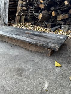 a wooden bench sitting in front of a pile of firewood next to a building