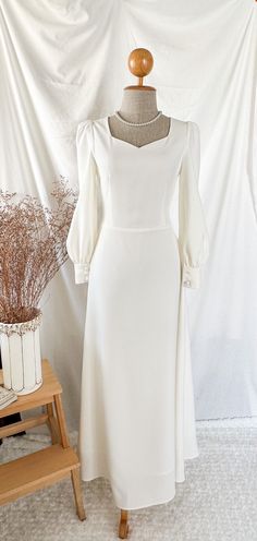 a white dress is on display in front of a white wall and a wooden table