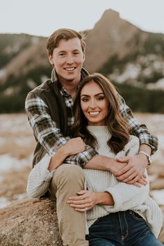 a man and woman sitting on top of a rock