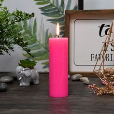 a pink candle sitting on top of a wooden table next to rocks and greenery