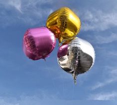 three metallic balloons floating in the air against a blue sky with wispy clouds