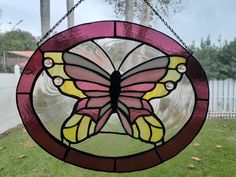 a stained glass butterfly hanging from a chain on a window sill in the yard