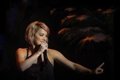 a woman holding a microphone in her right hand and wearing a black dress with sequins on it