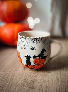 a coffee cup decorated with witches and pumpkins on a wooden table next to oranges