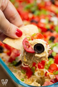 a hand holding a tortilla chip with black olives and tomatoes