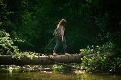 a woman walking across a fallen log over a river