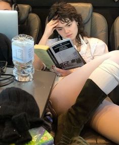 a woman sitting on a couch with her legs crossed and reading a book in front of her