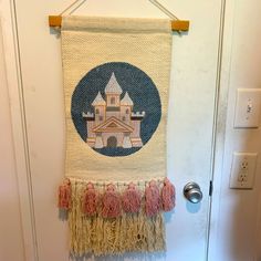 a wall hanging with a castle in the middle and pink tassels on it