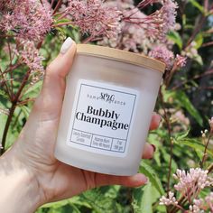 a hand holding a jar of bubbley champagne in front of some pink flower bushes