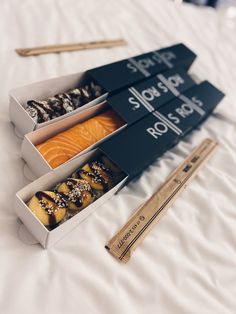 three sushi boxes are on the bed with chopsticks