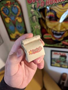 a person holding up a small candy bar in front of a wall with pictures on it