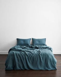 a bed with blue sheets and pillows in a white room next to a wooden floor