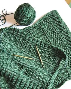 a green knitted sweater next to some knitting needles