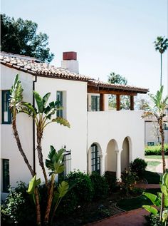 a white house with palm trees in front of it and a brick walkway leading up to the building