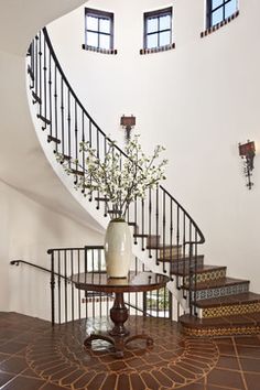 a vase with flowers sitting on top of a table in front of a spiral staircase