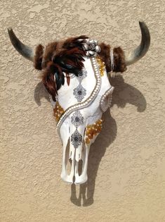 a cow's head is adorned with feathers and beads on the wall in front of a stucco wall